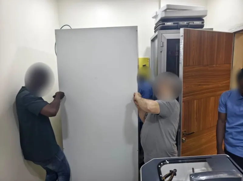 An installation team carrying a cabinet into a hospital room